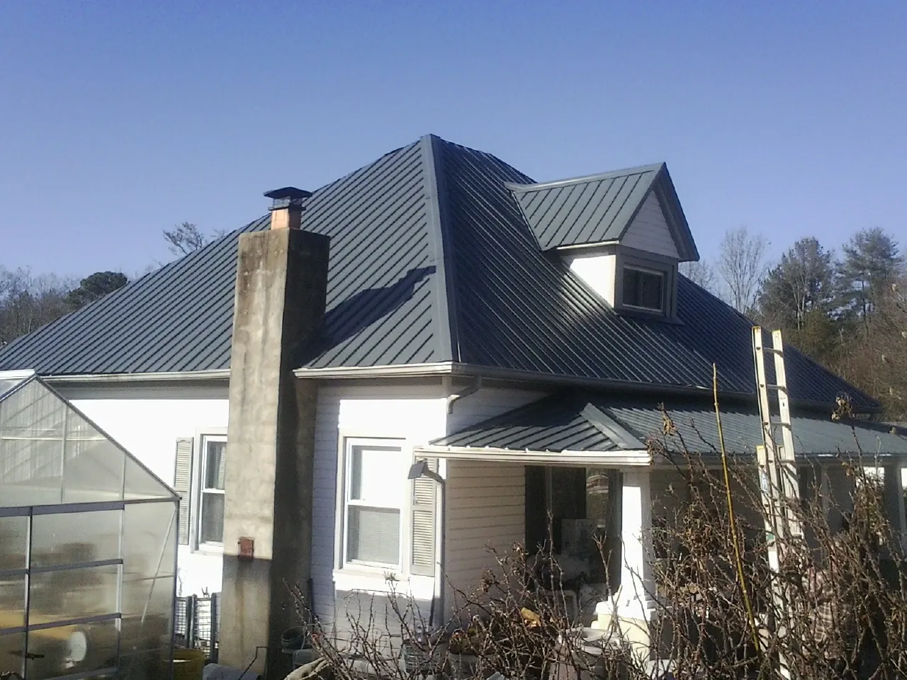 Dark blue standing seam metal roof on a white farmhouse with dormer — Slate & Tile Roof Repair by Roofing Brothers in Young America