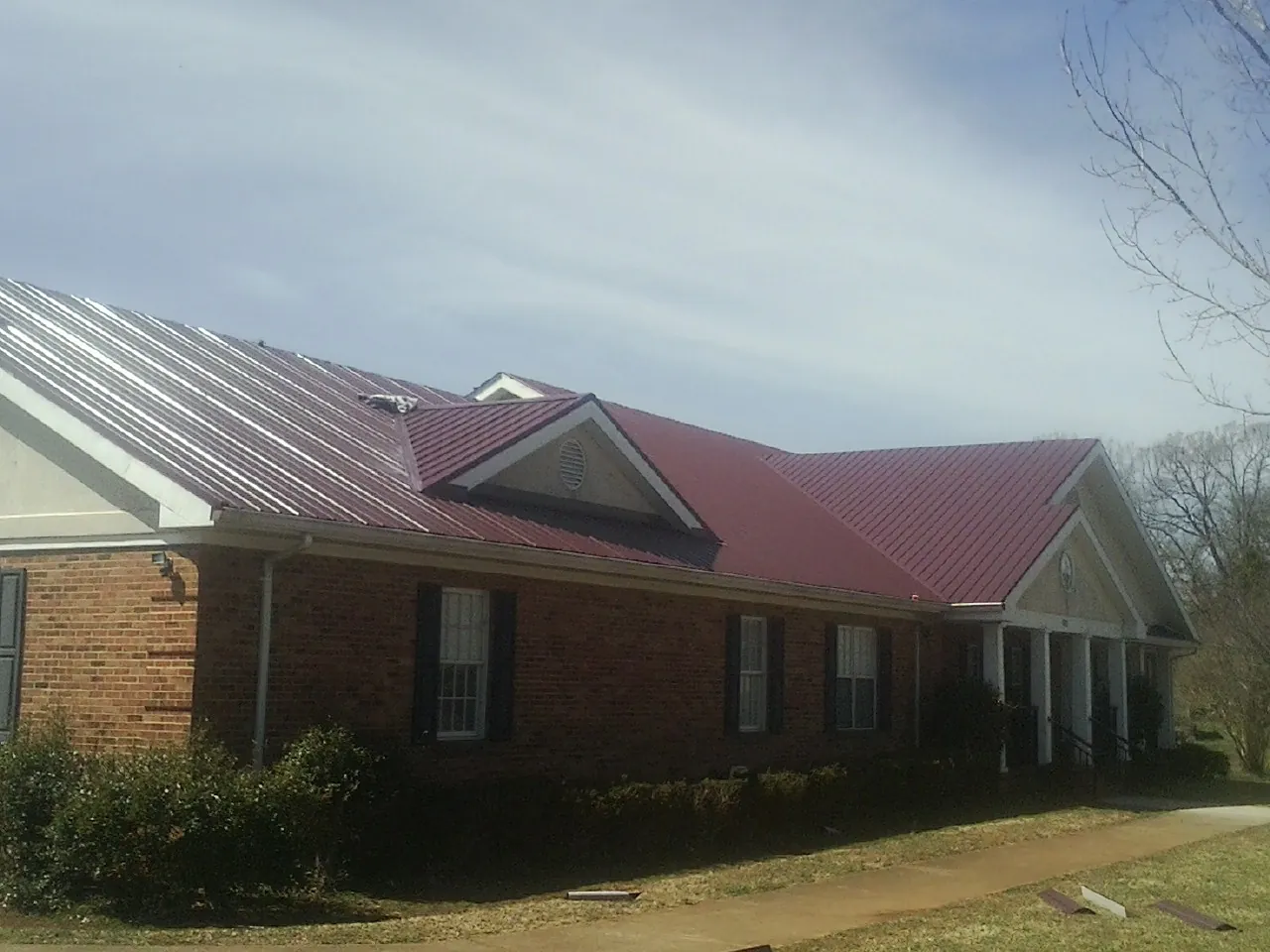 Red metal roof with gabled entries on a long brick building, from a Hail Damage Roof Repair job in Young America