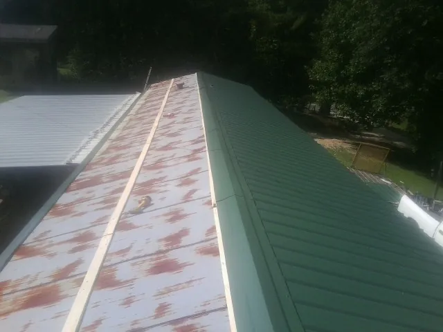 Old rusted panels beside newly installed green metal roofing — Wind Damage Roof Repair by Roofing Brothers in Young America