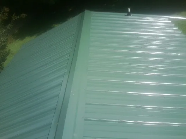 New green metal panels meeting at the ridge of a roof — Flat Roof Repair work by our crew in Young America