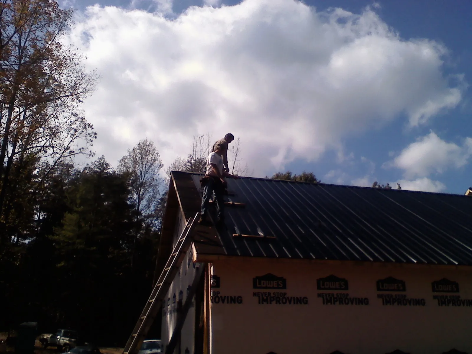 Roofer fastening dark metal panels high against a cloudy sky, from a Roof Inspection job in Young America