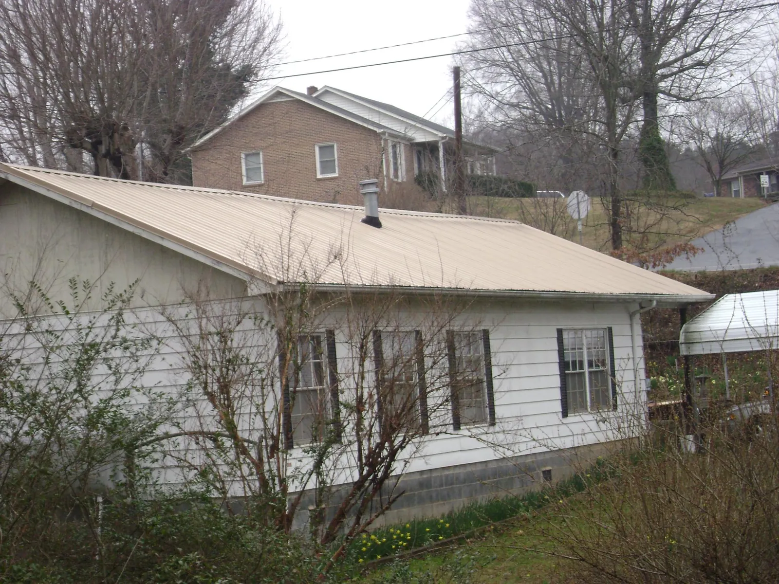 Tan metal roof on a white sided house set into a hillside — Commercial Roofing by Roofing Brothers in Young America